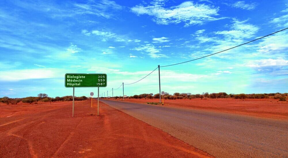Une route dans le désert avec un panneau de distance: biologiste = 365, médecin = 589, hôpital = 1500