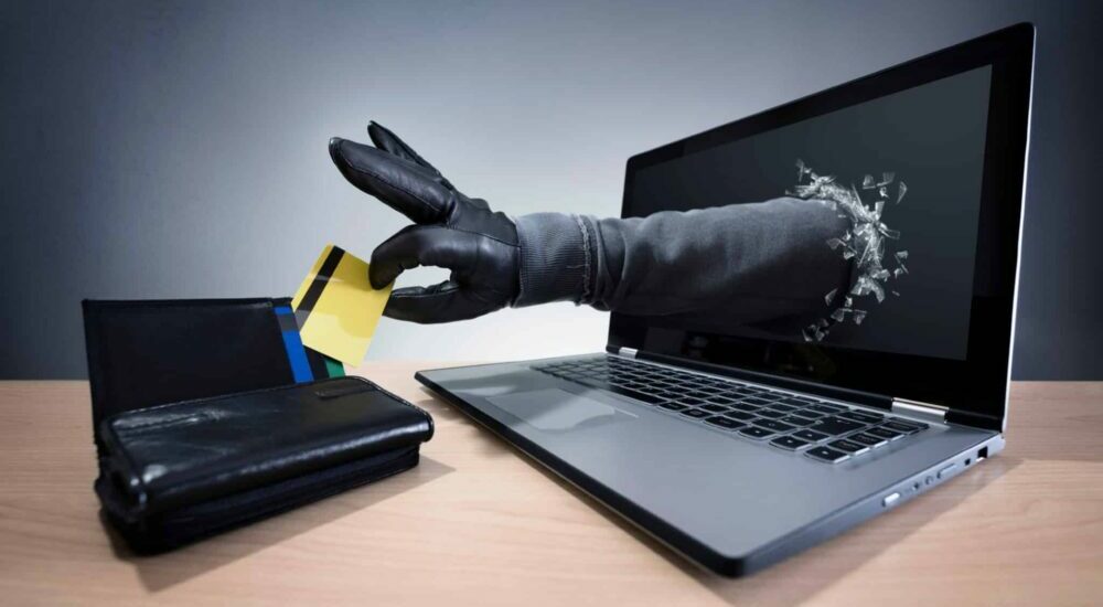 une main traverse un écran d'ordinateur pour voler une carte bancaire