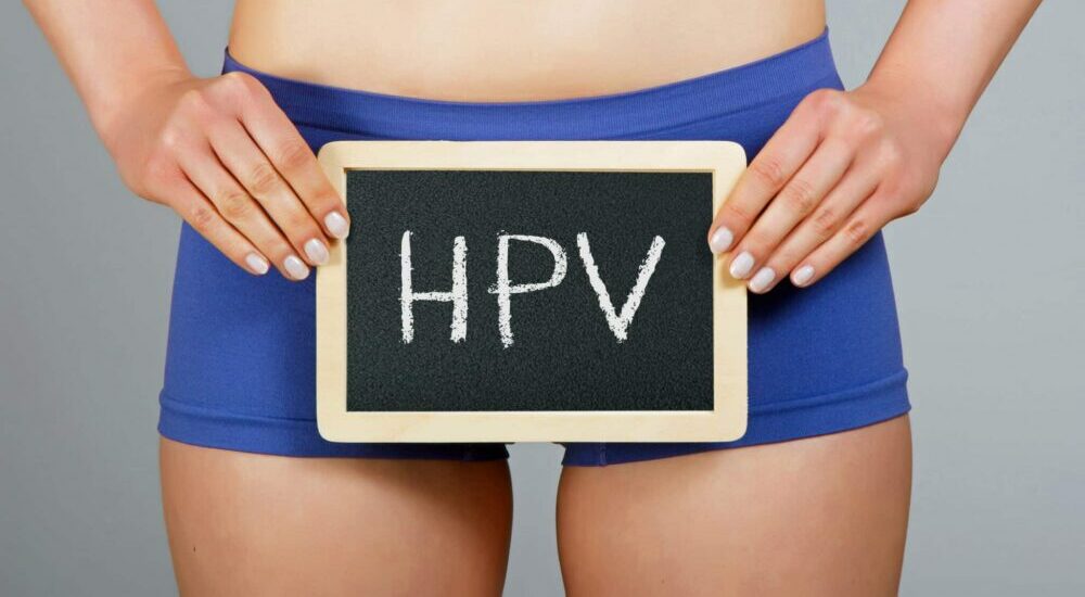 une femme en boxer tenant une ardoise devant elle. Sur l'ardoise est écrit "HPV"